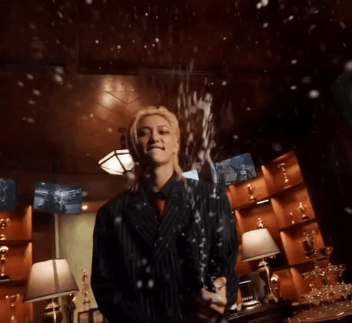 A Woman In A Suit Is Holding A Bottle Of Champagne In A Room . GIF