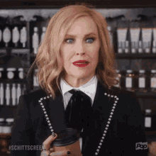 A Woman In A Suit Is Holding A Cup Of Coffee In Her Hand . GIF