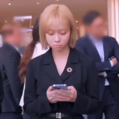 a woman in a suit is looking at her cell phone while standing in a crowd of people .