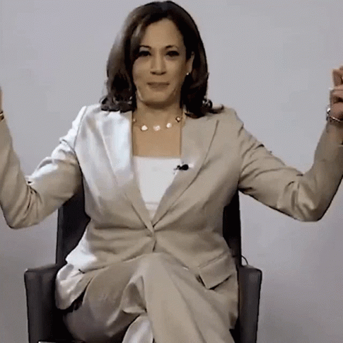 A Woman In A Suit Is Sitting In A Chair With Her Arms Outstretched GIF