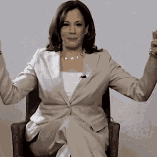 A Woman In A Suit Is Sitting In A Chair With Her Arms Up . GIF