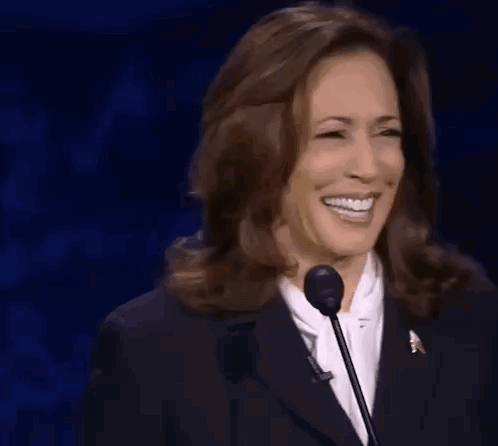 A Woman In A Suit Is Smiling While Standing In Front Of A Microphone . GIF