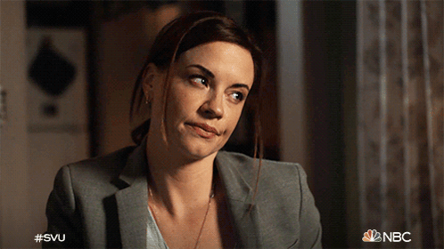 A Woman In A Suit Is Smiling With The Nbc Logo In The Background GIF