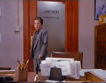 A Woman In A Suit Is Standing In Front Of A Door That Says ' Jacobi89 ' On It . GIF