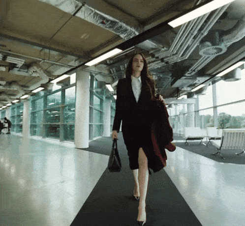 a woman in a suit is walking down a hallway holding a purse