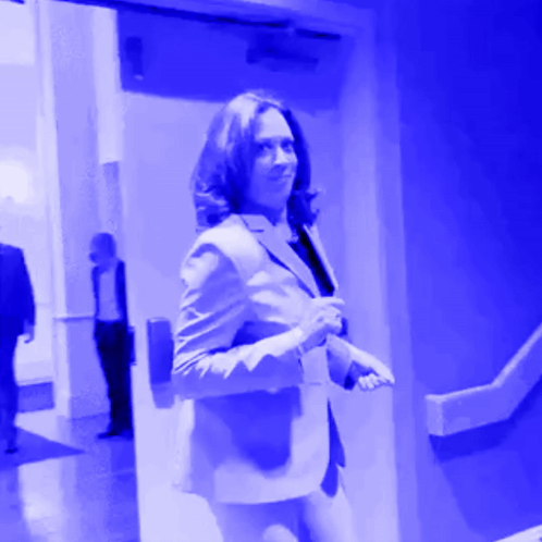 A Woman In A Suit Is Walking Through A Blue Door GIF