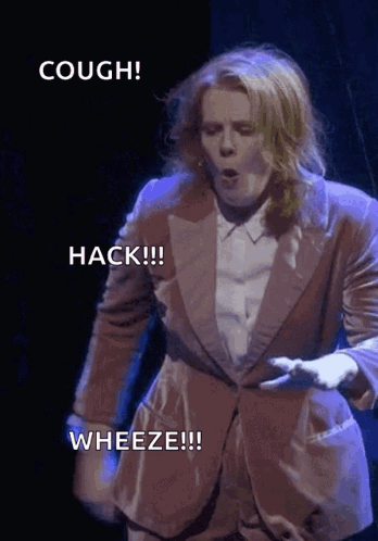 A Woman In A Suit Says Hack Wheeze And Cough On A Stage GIF