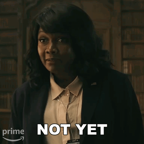 A Woman In A Suit Says " Not Yet " In Front Of A Bookshelf GIF