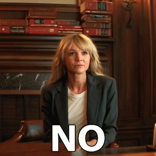 A Woman In A Suit Sits At A Desk With The Word No Written On Her Face GIF