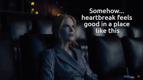 A Woman In A Suit Sits In A Dark Room With The Words " Somehow Heartbreak Feels Good In A Place Like This " Above Her GIF