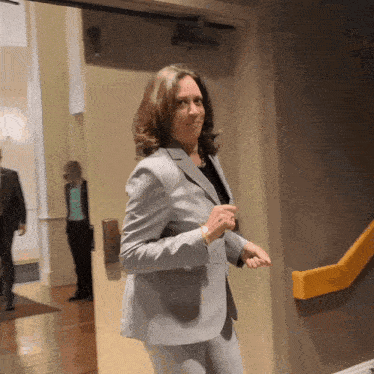A Woman In A Suit Stands In A Hallway GIF