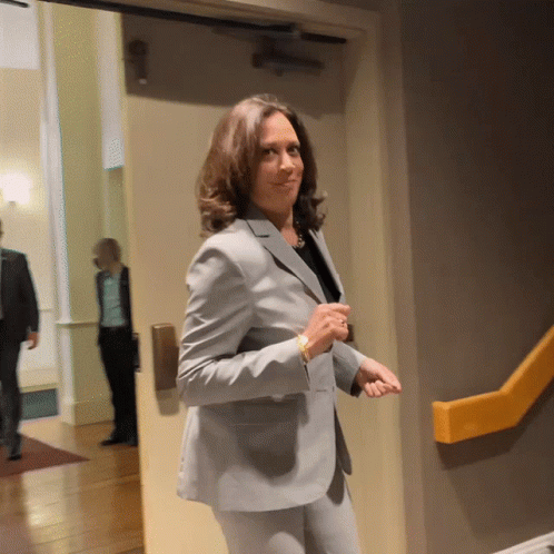 A Woman In A Suit Stands In A Hallway GIF