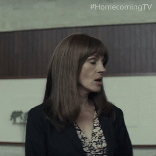 A Woman In A Suit Stands In Front Of A Wooden Wall With #Homecoming Tv Written On The Bottom GIF