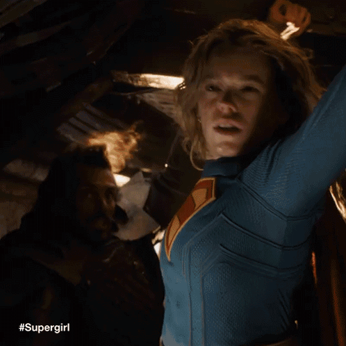 A Woman In A Supergirl Costume Is Holding A Light In Her Hand . GIF