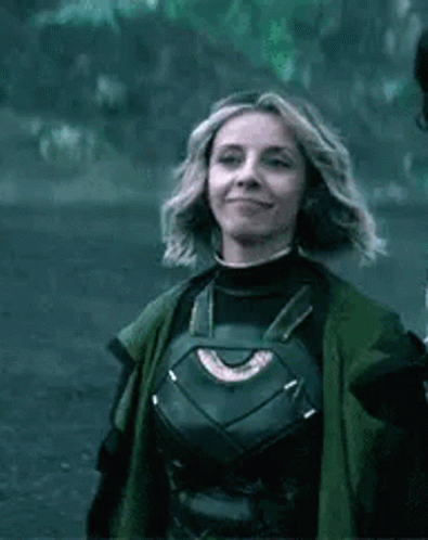 A Woman In A Superhero Costume Is Smiling And Wearing A Green Coat . GIF
