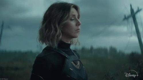 A Woman In A Superhero Costume Is Standing In A Field With A Telephone Pole In The Background . GIF