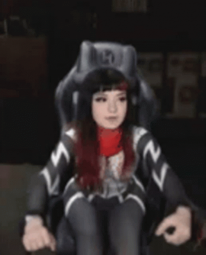 A Woman In A Superhero Costume Is Standing In Front Of A Chair . GIF