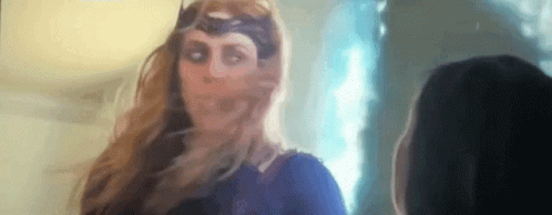 A Woman In A Superhero Costume Is Standing Next To Another Woman In A Room . GIF