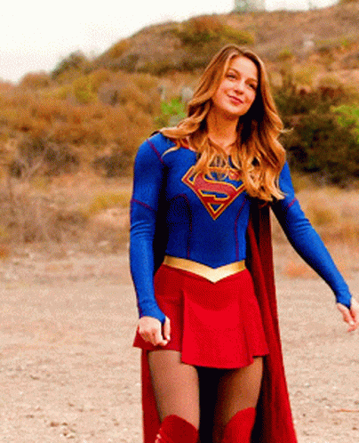 A Woman In A Superman Costume Is Standing In A Dirt Field GIF