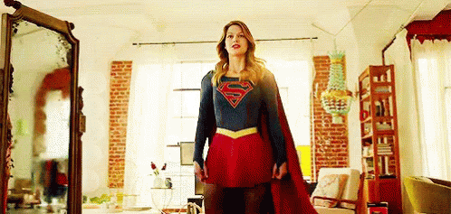 A Woman In A Superman Costume Is Standing In Front Of A Mirror . GIF