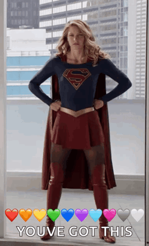 A Woman In A Superman Costume Is Standing In Front Of A Window With Her Hands On Her Hips .. GIF