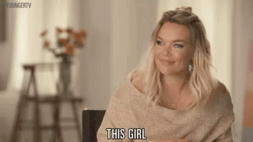 A Woman In A Sweater Is Sitting In A Chair And Smiling While Saying This Girl . GIF
