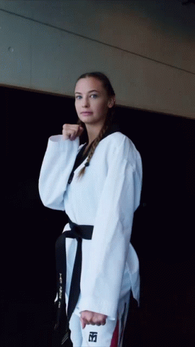 A Woman In A Taekwondo Uniform Holds A Black Belt With The Letter T On It GIF