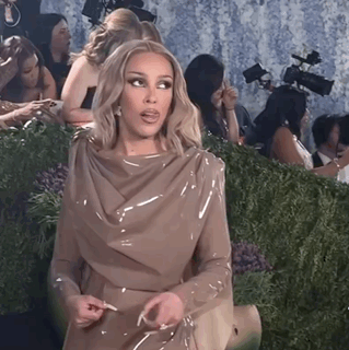 A Woman In A Tan Dress Is Sitting In Front Of A Group Of People GIF