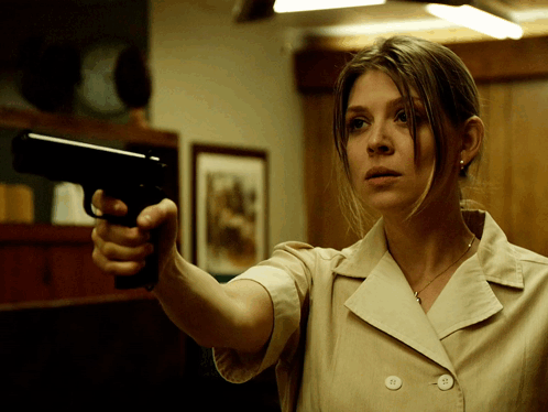 A Woman In A Tan Jacket Is Pointing A Gun GIF