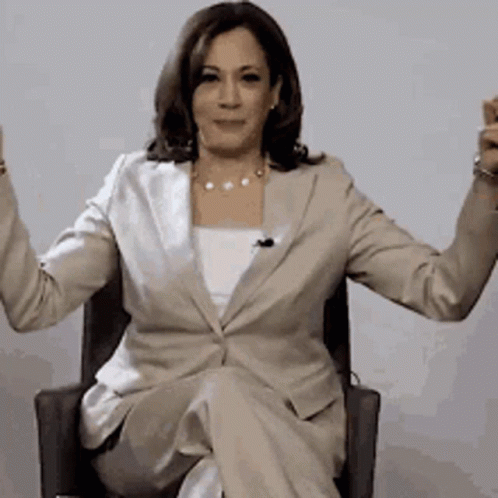 A Woman In A Tan Suit Is Sitting In A Chair With Her Arms Outstretched GIF