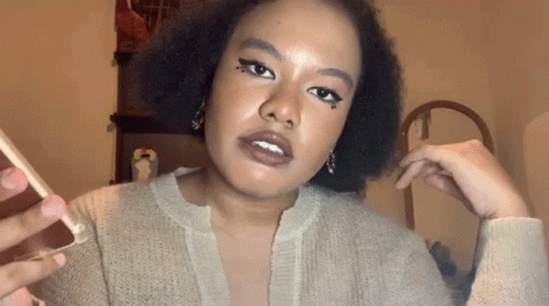 A Woman In A Tan Sweater Is Holding A Cell Phone GIF
