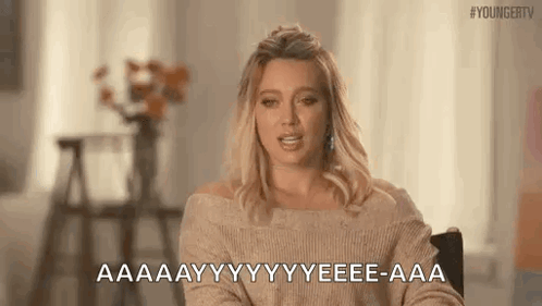 A Woman In A Tan Sweater Is Sitting In A Chair And Talking . GIF