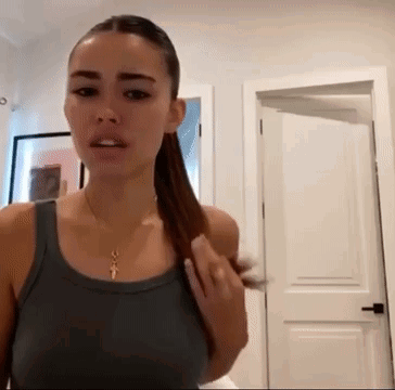 A Woman In A Tank Top Is Standing In Front Of A Door . GIF
