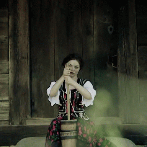 A Woman In A Traditional Costume Is Sitting On A Wooden Bucket GIF