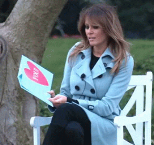 A Woman In A Trench Coat Is Sitting On A Bench Holding A Piece Of Paper That Says " You " GIF