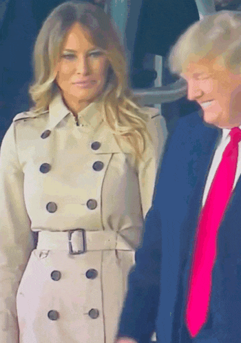 A Woman In A Trench Coat Stands Next To A Man In A Blue Suit GIF