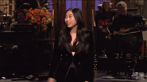 A Woman In A Tuxedo Is Singing On Stage In Front Of A Band GIF