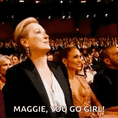 A Woman In A Tuxedo Is Sitting In Front Of A Crowd At A Awards Show . GIF