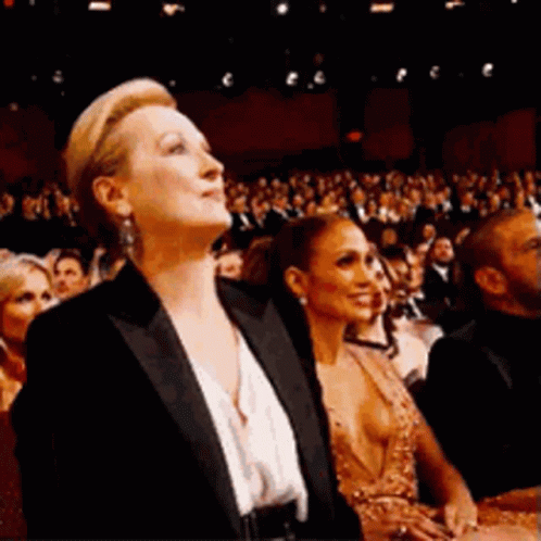 A Woman In A Tuxedo Is Sitting In Front Of A Crowd Of People . GIF