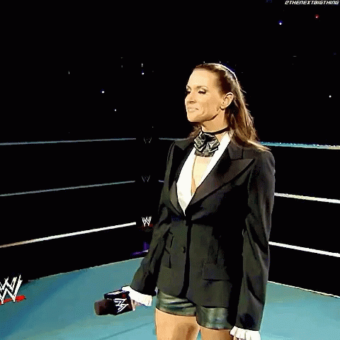 A Woman In A Tuxedo Stands In Front Of A Sign That Says Wrestlemania Principal Owner Of Stephanie Mcmahon GIF