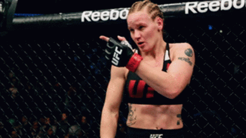 A Woman In A Ufc Top Stands In A Cage GIF