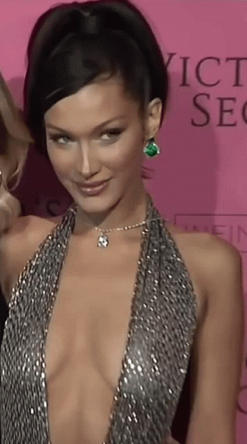 A Woman In A Very Plunging Dress Is Standing In Front Of A Pink Background That Says Victoria 'S Secret GIF
