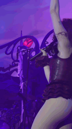 A Woman In A Very Revealing Outfit Is Singing Into A Microphone On Stage GIF