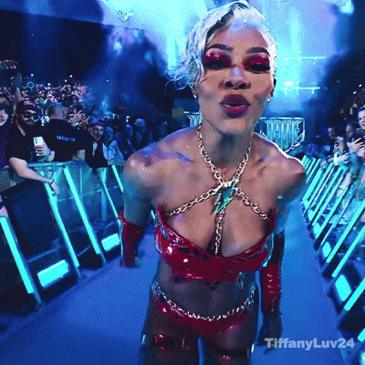 A Woman In A Very Revealing Outfit Is Standing In Front Of A Crowd With Tiffanyluv24 On The Bottom Right GIF