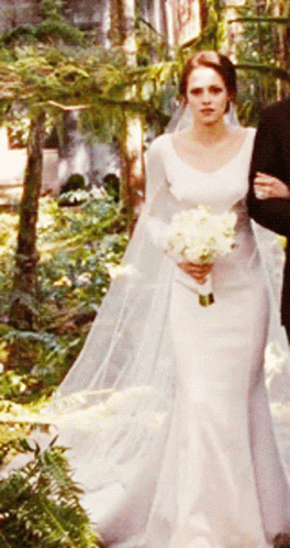 A Woman In A Wedding Dress Holding A Bouquet Of Flowers GIF