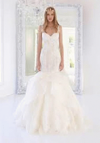 A Woman In A Wedding Dress Is Standing In Front Of A Window In A Room . GIF