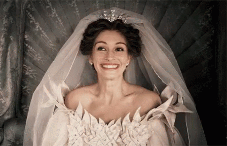 A Woman In A Wedding Dress With A Veil And Tiara Is Smiling . GIF
