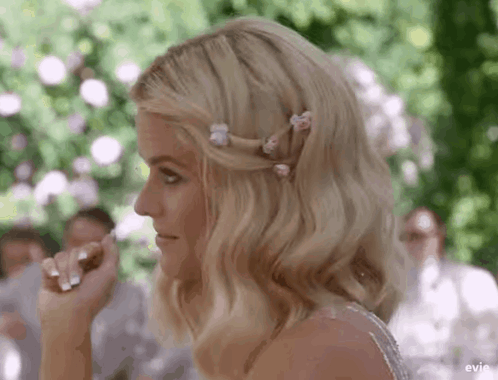 A Woman In A Wedding Dress With Flowers In Her Hair Is Sitting At A Table . GIF