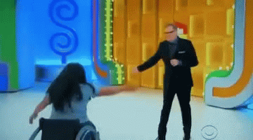 A Woman In A Wheelchair Is Dancing In Front Of A Man In A Suit GIF