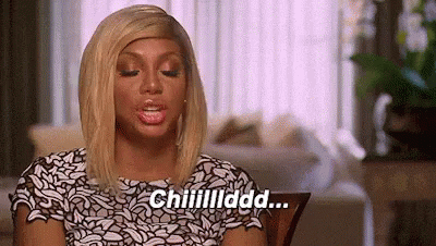A Woman In A White And Black Dress Is Sitting In A Living Room Talking . GIF